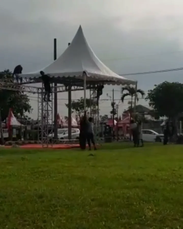Tenda putih dan rangka truss sedang dipasang di lapangan
